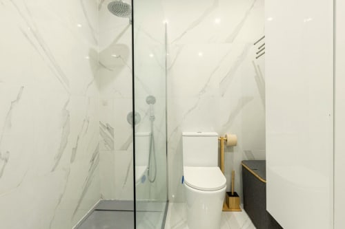 Modern bathroom with marble walls, rainfall shower, toilet, and wooden towel rack at Sea'Ya Cascais apartment in Cascais