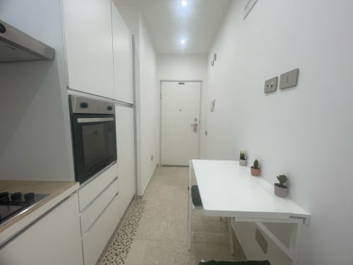 Cucina moderna nell'appartamento Dream Suite Bologna con mobili bianchi, forno nero, tavolo da pranzo bianco e piante in vaso