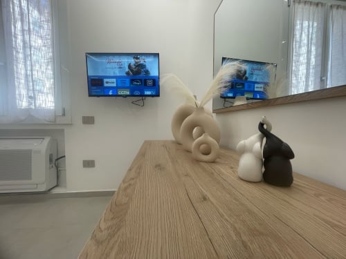 Zona living moderna con scrivania in legno, sculture decorative, TV a parete e specchio presso Dream Suite Bologna