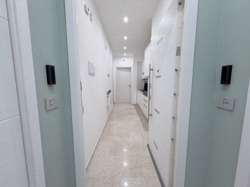 Corridoio con cucina a galera moderna alla Dream Suite Bologna: mobili bianchi, pareti verde salvia e pavimento in cemento levigato