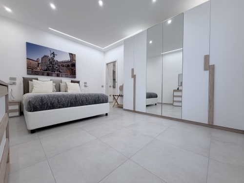Camera King Deluxe moderna presso Dream Suite Bologna con letto bianco, armadio specchiato e pavimentazione in piastrelle