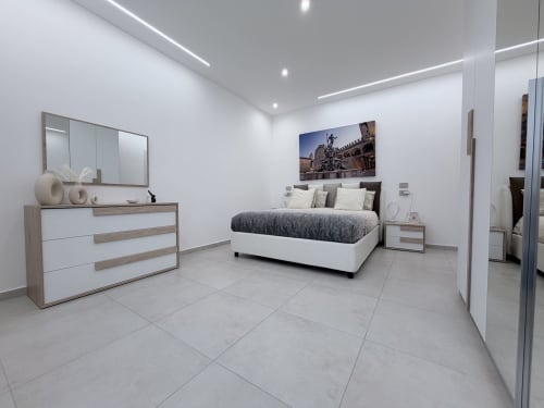 Camera da letto moderna Dream Suite Bologna con pareti bianche, pavimento piastrellato, arredi contemporanei e opere d'arte urbana