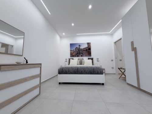 Camera da letto moderna presso Dream Suite Bologna con pareti bianche, letto contemporaneo, cassettone in legno e pavimento piastrellato