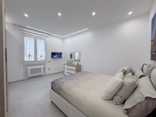 Camera moderna della Dream Suite Bologna con letto king size, TV a schermo piatto, cassettone in legno e arredamento minimalista bianco