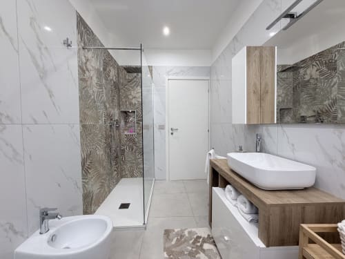 Bagno moderno nella Dream Suite Bologna con pareti in marmo, doccia walk-in e vanità in legno con lavabo bianco.