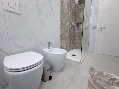 Bagno moderno nella Dream Suite Bologna con vaso, bidet, lavabo rotondo e doccia con box in vetro e piastrelle decorative