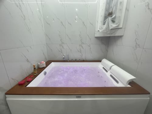 Vasca idromassaggio lussuosa con acqua viola e getti nel Dream Suite Bologna, bagno rivestito in marmo con vasca in legno