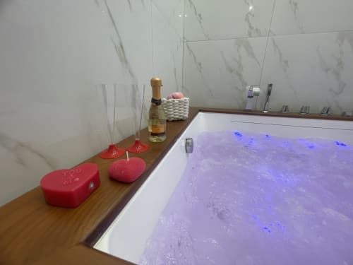 Vasca idromassaggio lussuosa con getti blu nella Dream Suite Bologna, mensola in legno con champagne, candele e amenities spa