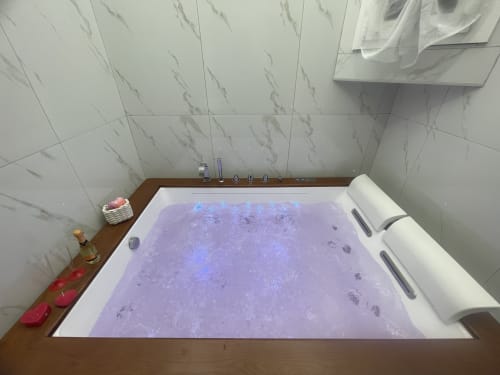 Vasca idromassaggio di lusso con getti illuminati di viola alla Dream Suite Bologna, riempita di acqua frizzante e comfort spa su legno