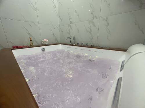 Vasca idromassaggio lussuosa nella Dream Suite Bologna con acqua viola e sali da bagno, pareti in marmo, design moderno