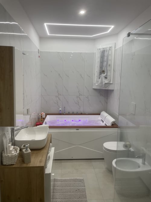 Bagno moderno della Dream Suite Bologna con piastrelle in marmo, vasca da bagno con illuminazione viola, lavabo da appoggio, bidet e vetro
