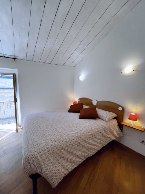 Camera luminosa nell'appartamento Nel Cuore di Lanciano, con letto in legno, lampade rosse, muri bianchi e porta verso la città