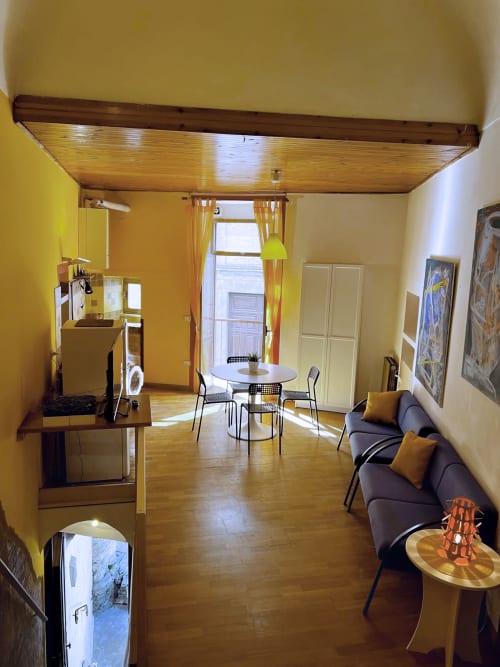 Luminoso appartamento giallo a Lanciano con soffitto in legno, tavolo da pranzo, divano grigio, angolo cottura e accesso al balcone sulla città