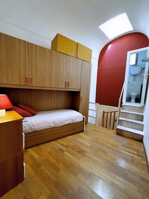 Camera moderna a WelcHome Lanciano con arredi in legno, letto, parete rossa e bagno ensuite