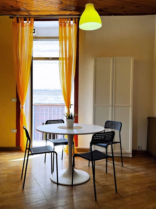 Zona pranzo moderna nell'appartamento WelcHome a Lanciano con tavolo rotondo bianco, sedie nere, lampada a sospensione gialla e vista sulla città