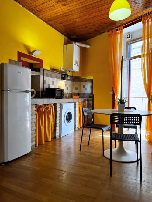 Zona cucina-soggiorno giallo brillante nell'appartamento WelcHome Lanciano con soffitto in legno, elettrodomestici bianchi, tavolo da pranzo