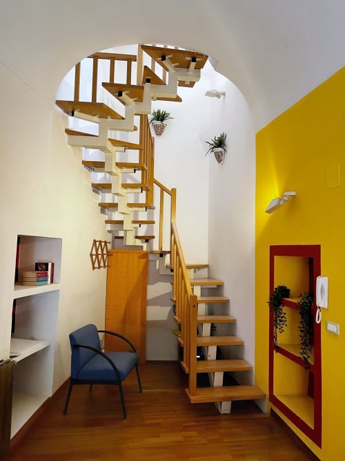 Moderna scala a spirale nell'appartamento WelcHome, Lanciano. Gradini in legno, pareti gialle e porta d'ingresso rossa.