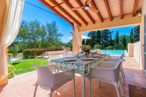 Patio comedor cubierto en villa Can Mantellé en Artà con vistas a la piscina, vigas de terracota y paisaje mediterráneo