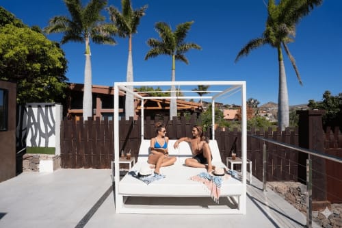 Dos huéspedes descansando en una cama con dosel blanco en Villa La Menta, Home Stay Gran Canaria, con vistas a palmeras y montañas