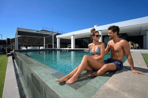 Pareja relajándose junto a la piscina de Villa La Menta, villa de lujo de Home Stay Gran Canaria con piscina turquesa y arquitectura moderna