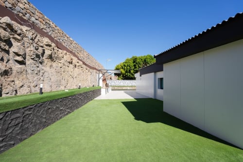 Villa blanca moderna con patio, jardín verde, muros de piedra antigua y tejado negro en Home Stay Gran Canaria