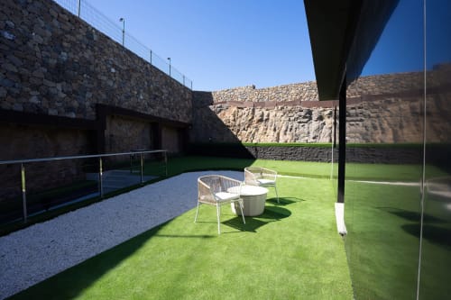 Patio contemporáneo con jardín cuidado, mobiliario blanco, muros de piedra y vistas a la montaña en Villa La Menta Gran Canaria