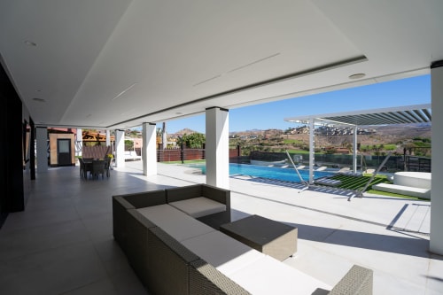 Amplia zona de descanso junto a la piscina de Villa La Menta, Home Stay Gran Canaria, con mobiliario moderno y vistas a las montañas.