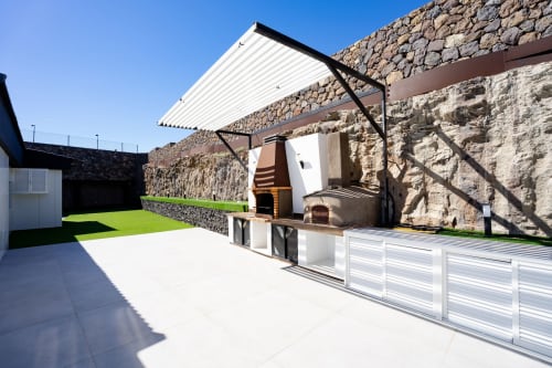 Patio exterior de Villa La Menta con muros de piedra, toldo retráctil moderno y parrilla en Las Palmas de Gran Canaria