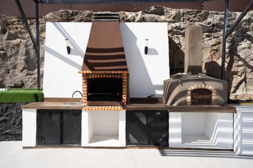Zona de cocina exterior en Villa La Menta, Gran Canaria con chimenea de ladrillo, horno de pizza y parrilla de acero inoxidable