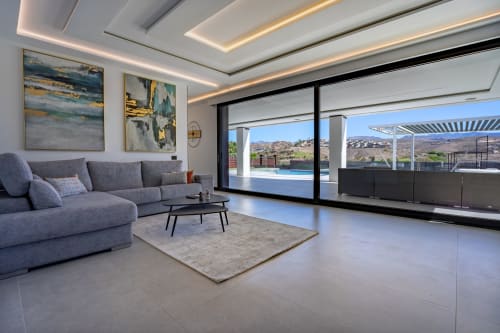 Sala moderna de villa con sofá gris, obras de arte y vistas panorámicas de piscina y paisaje de Gran Canaria