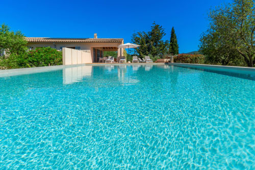 Piscina cristalina de la villa Massa Properties en Artà, España, con tumbonas y casa mediterránea