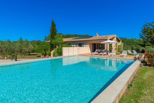 Villa de lujo en Artà con piscina turquesa resplandeciente, tumbonas y jardines mediterráneos bajo cielo azul despejado