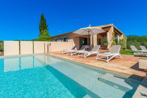 Villa de lujo en Artà con piscina turquesa, tumbonas y patio de terracota bajo cielo azul despejado