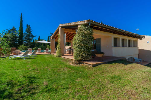 Villa toscana en Artà con pérgola de terracota, jardín exuberante, tumbonas y muros cubiertos de hiedra bajo cielo azul despejado