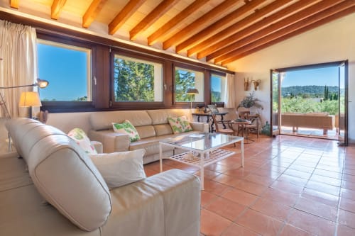 Amplia sala de estar en Massa Properties de Artà con muebles color crema, vigas de madera, baldosas de barro y vistas panorámicas