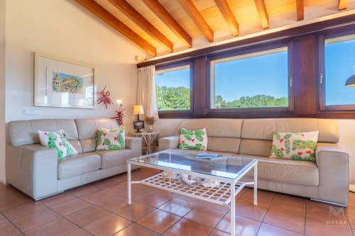 Sala de estar moderna con sofás beige, mesa de centro de cristal y ventanales panorámicos con vistas al campo de Artà en Massa
