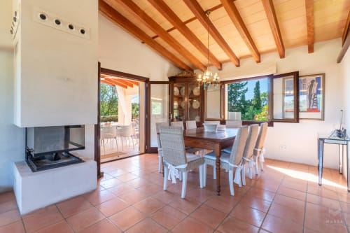 Amplio comedor en Artà con vigas de madera, chimenea y suelos de terracota con vistas al paisaje mediterráneo