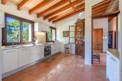 Cocina moderna con armarios blancos, vigas de madera y baldosas de terracota en Massa Properties en Artà