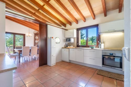 Cocina moderna con muebles blancos, vigas de madera y suelos de terracota en Massa Properties, Artà, España