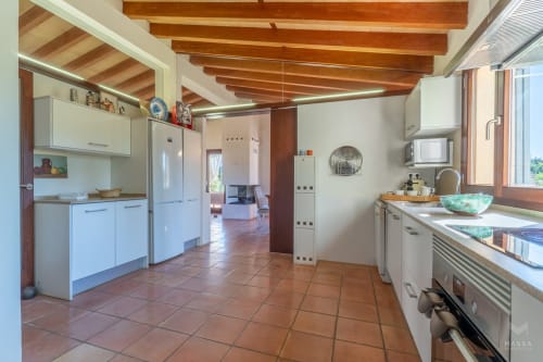 Amplia cocina con muebles blancos, vigas de madera y azulejos de terracota en alquiler vacacional en Artà, Mallorca