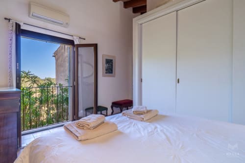 Luminosa habitación en Artà, España con vistas al mar, ropa de cama blanca, toallas dobladas y balcón abierto con vistas al campo