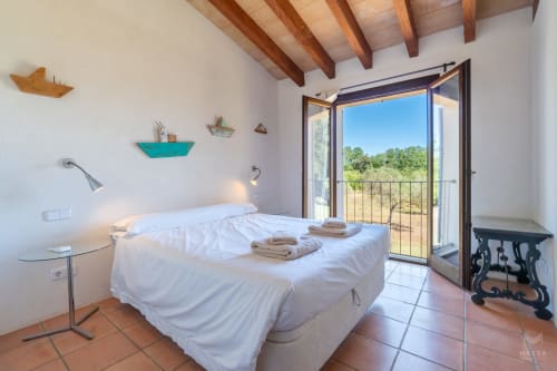 Dormitorio luminoso con vigas de madera, ropa de cama blanca y terraza con vistas a la campiña de Artà en Massa Properties
