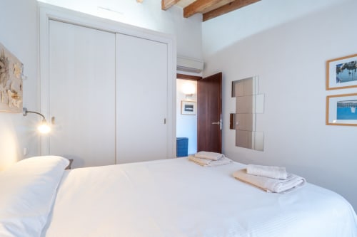 Dormitorio luminoso en Massa Properties de Artà con cama blanca, vigas de madera y comodidades modernas