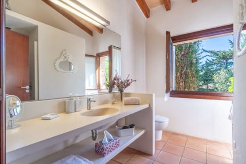 Baño luminoso en Massa Properties, Artà, con lavabo moderno, espejo grande, suelos de terracota y vistas al jardín