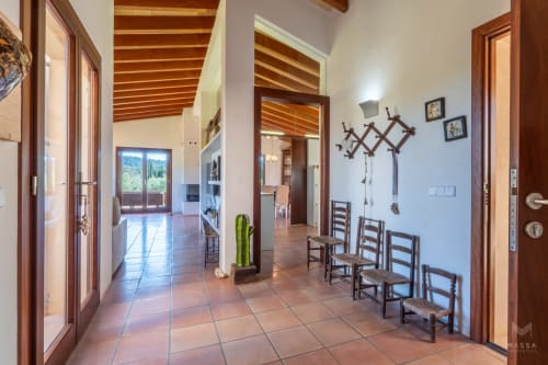Amplio vestíbulo de hotel en Artà con suelos de terracota, vigas de madera, sillas rústicas y luz natural de puertas de cristal