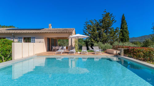 Villa de lujo en Artà con piscina reluciente, tumbonas, sombrilla y jardines mediterráneos bajo cielo despejado