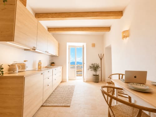 Bright Tuscan kitchen and dining area with wooden beams, white cabinetry, and garden view doors in Montemassi