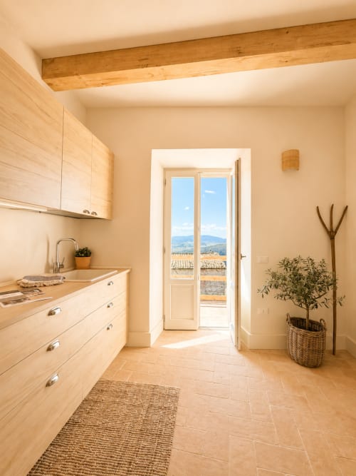 Bright Tuscan kitchen with wooden beams, light wood cabinetry, and French doors opening to countryside views at Montemassi