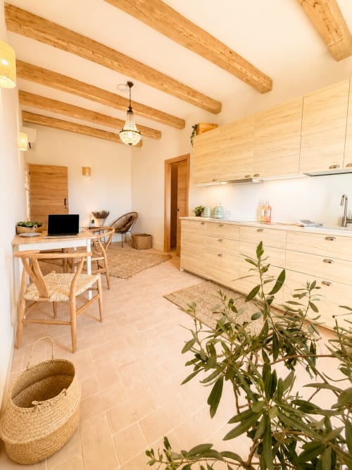 Bright open-plan kitchen and workspace at Tuscan Townhouse with wooden beams, light wood cabinetry, and garden view in