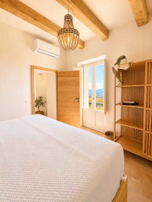 Bright bedroom in Tuscan Townhouse with queen bed, wooden beams, beaded chandelier, and terrace doors overlooking Montemassi